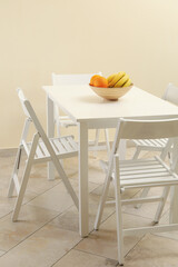 White table with fruits and folding chairs in kitchen room