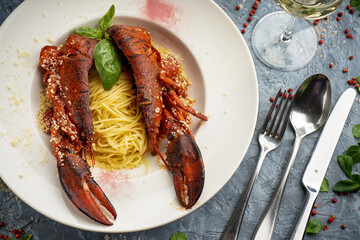 cooked sliced ​​lobster on a plate of pasta garnished with basil leaf on gray background
