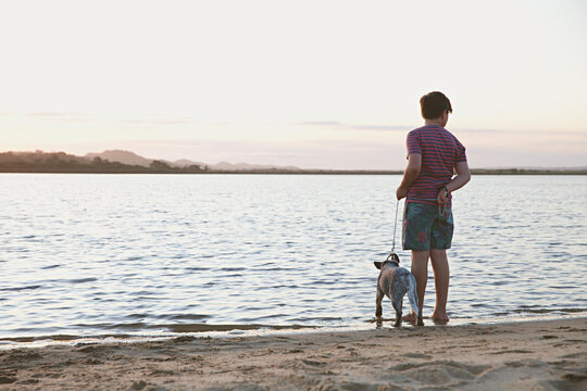 A young boy at the beach during sunset with his puppy