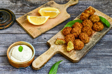 Fresh vegan dish-  falafel balls from spiced chickpeas  with lemon   and garlic yogurt sauce  on wooden rustic table.