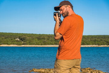 Photographer in t-shirt and cargo pants walking around sea shore with mirror less camera, shooting nature, half body portrait, landscape photography concept