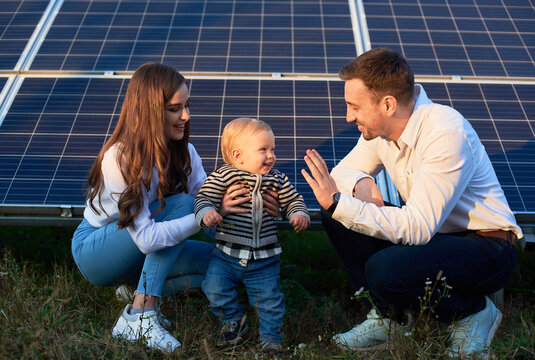 Dad, Mom And Baby On The Background Of Solar Panels On A Warm Day. The Concept Of Family Warmth And Comfort In The Modern World With Continuously Advancing Technology