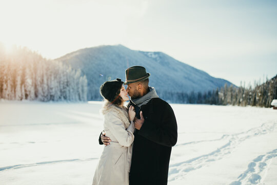 Young mixed couple embrace in love on snow covered winter lake