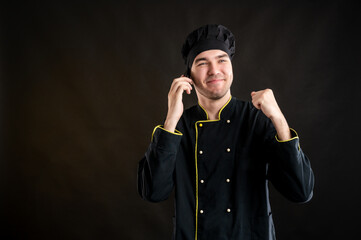 Young male dressed in a black chef suit happy face and gestures and talking on cellphone