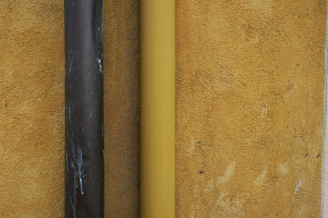 yellow ochre plastered wall with two drainpipes, brown and yellow