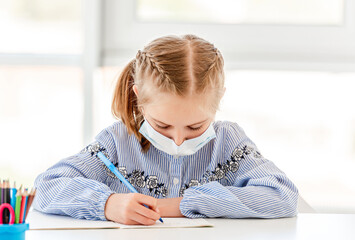 Naklejka premium Schoolgirl in protective mask writing in notebook