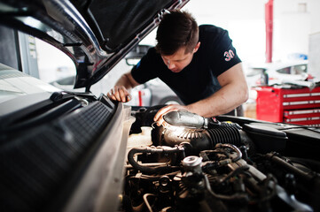 Car repair and maintenance theme. Mechanic in uniform working in auto service, checking engine.