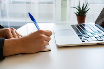 there is a laptop on the table next to a girl making notes in the diary