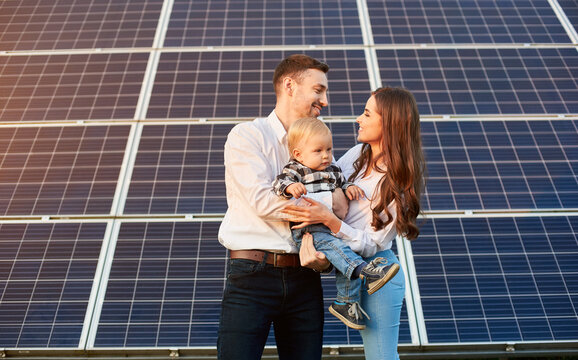 Young family with a small child in her arms on a background of solar panels. A man and a woman look at each other with love. Solar energy concept image