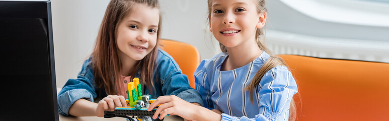 Website header of schoolgirls looking at camera while holding robot in classroom of stem school © LIGHTFIELD STUDIOS