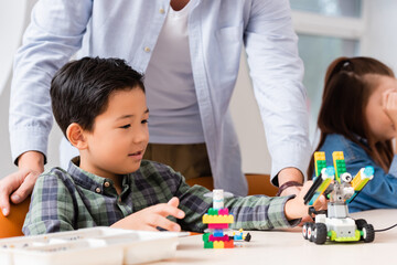 Selective focus of teacher standing near asian schoolboy modeling robot in stem school © LIGHTFIELD STUDIOS