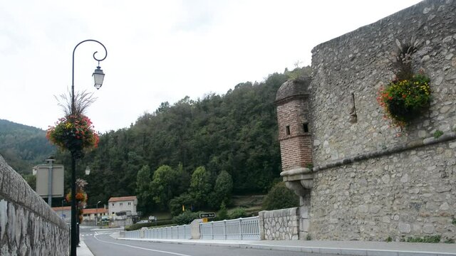 Still image of the fortress of Prats de Mollo la Preste. From this angle you can see the entrance road, the bridge where the Tec river passes, a lamppost with red flowers and a part of the fortress.
