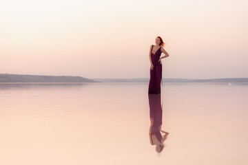 A beautiful young woman posing at sunset in the water with a reflection