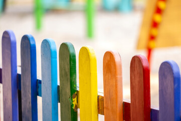 Part of wooden, rainbow colorful painted fence  on a sunny hot summer day in a city park.