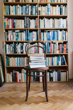 A classic chair with a pile of books in front of a bookcase