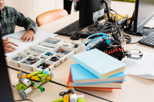 Selective focus of schoolboy sitting near parts of robots and computers in school