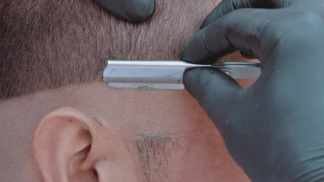 Barbero afeitando patilla con navaja a modelo masculino en barber shop