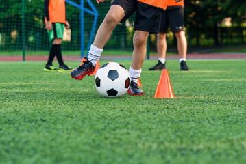 Close up teen boy in sportswear trains soccer at stadium and learns to circle the ball between training orange cones.