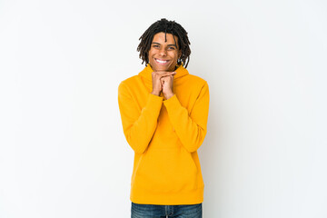 Young african american rasta man keeps hands under chin, is looking happily aside.