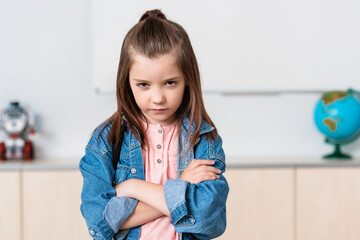 Confident schoolchild with crossed arms looking at camera in classroom