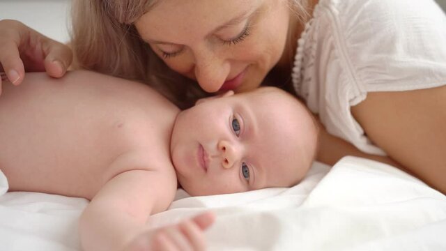 mother lies with baby in bed and kisses. concept of maternal love, newborn care.