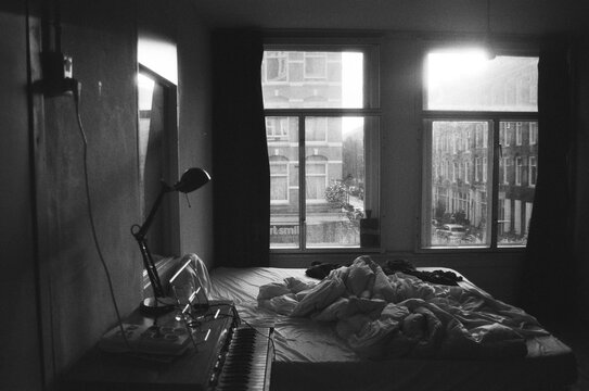 A black and white film photo of disordered bedroom with a piano