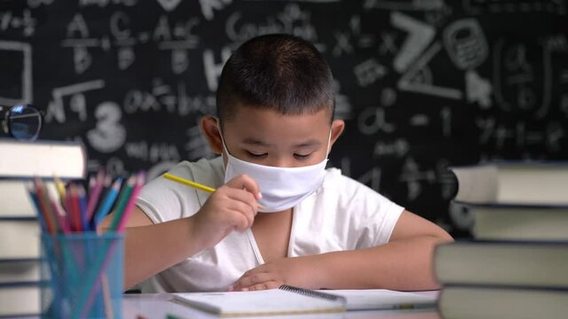 A boy wearing a mask is learning to write letters.