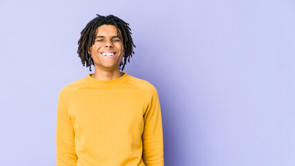 Young black man wearing rasta hairstyle laughs and closes eyes, feels relaxed and happy.