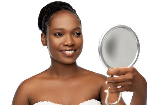 beauty and people concept - portrait of happy smiling young african american woman with bare shoulders looking to mirror over white background