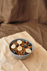 Homemade granola in a plate with nuts, honey, blueberries, banana and other natural ingredients served on napkin over brown background