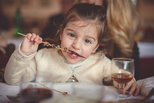 A cute child eating a meat skewer