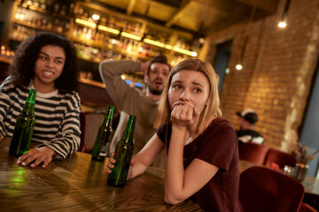 Friends looking disappointed while watching sports match on TV together, drinking beer and cheering for team in the bar. People, leisure, friendship and entertainment concept