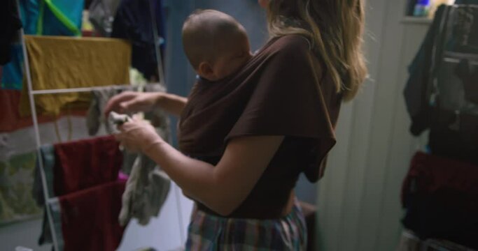 A young mother is trying to hang the washing whilst carrying her baby in a sling