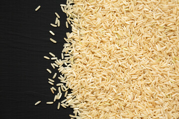 Dry Brown Rice on a black background, top view. Overhead, from above. Copy space.