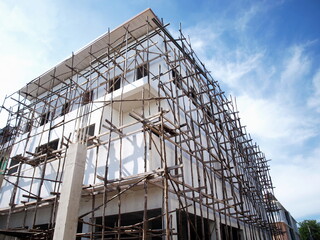 Wooden scaffolding with white townhouses. Wooden frame during the construction of the house in the lower corner On the blue sky background there are white clouds outdoors. Selective focus