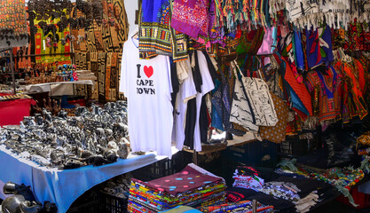 Fototapeta na wymiar Cape Town, South Africa - 11/12/2019: Typical souvenir street market with shirts, colorful bags, dresses and textiles