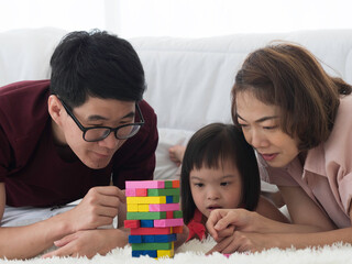 Obraz na płótnie Canvas Asian parents playing with colorful blocks with disabled child or down syndrome or trisomy 21 daughter in the bedroom. Happy family concept.