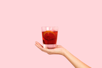 Mano femenina sosteniendo un vaso con cocktail sobrte un fondo rosa pastel liso y aislado. Vista defrente. Copy space