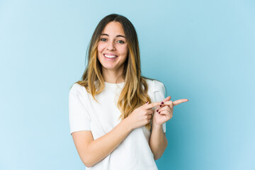 Young caucasian woman isolated on blue background excited pointing with forefingers away.