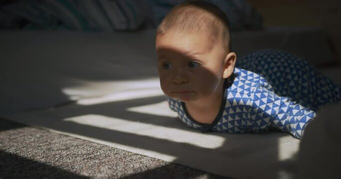 A little baby on his belly is trying to crawl on the floor