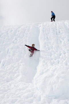 Boy flies down a snowy chute while mom looks on from the top of the hill