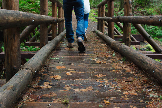 feet of couple walking across rustic pole bridge in mountains
