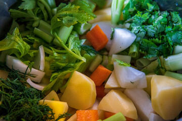 Fresh uncooked ingredients of vegetables and root veggies in a pot for cooking vegetables soup / stock. Potatoes, onions carrots, celery, leek, coriander, parsley and dill. top view