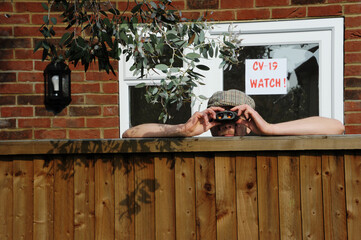 Nosy neighbor peeking over the fence, spying on his neighbours during the covid-19 lockdown