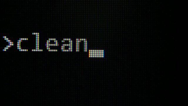 Command line with word Clean typed on computer screen closeup . Macro detail shot monitor pixels. Pixels zoomed in with white glowing crystals on a black background.