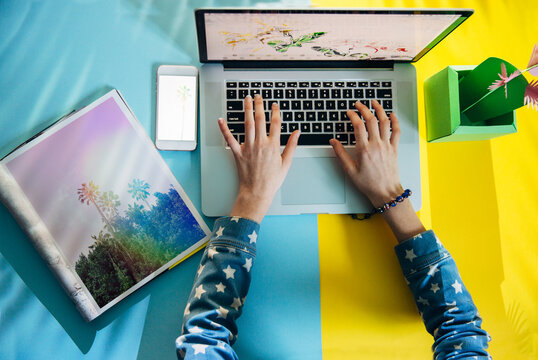 Female hands working on laptop with various objects on the desk