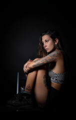 Whole body portrait, of a young woman, alternative, with tattoos, with a thoughtful look, lost in emptiness. Black background.