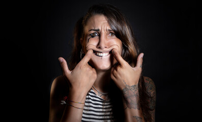 Portrait of an alternative teenager, with tattoos, forcing to smile, looking at the camera with a...