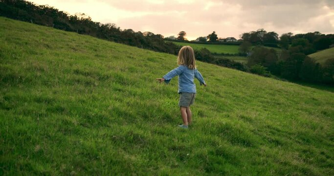 A preschooler is running and spinning in a field at sunset