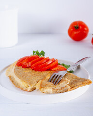 Oatmeal pancake with melted cheese and red tomato on white wooden background. Easy and quick breakfast.